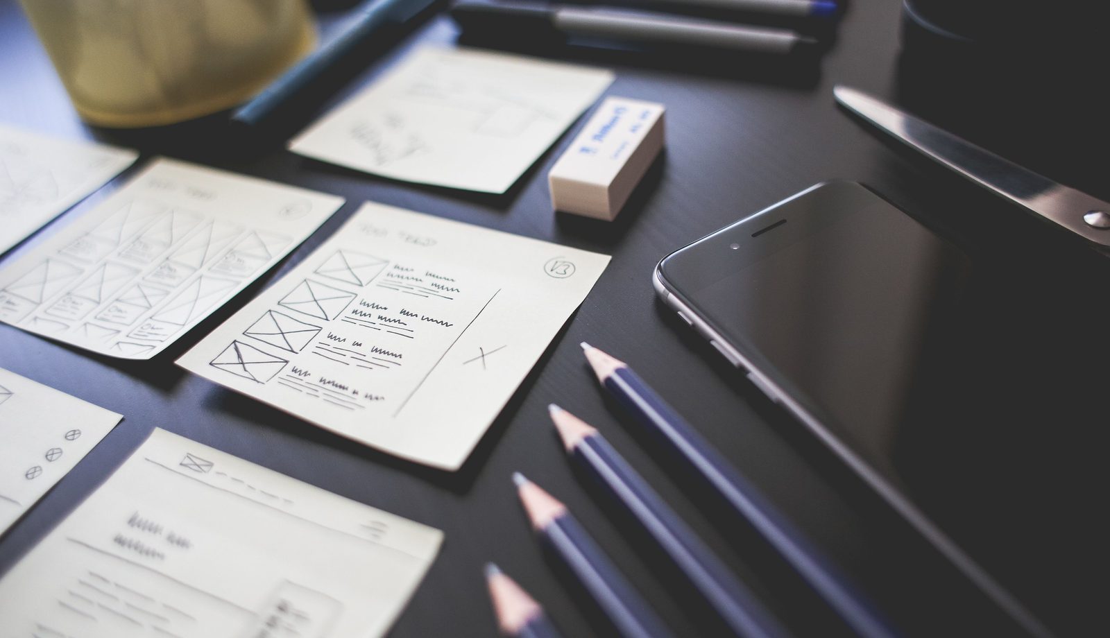 Hand-drawn app wireframes next to a phone on a desk